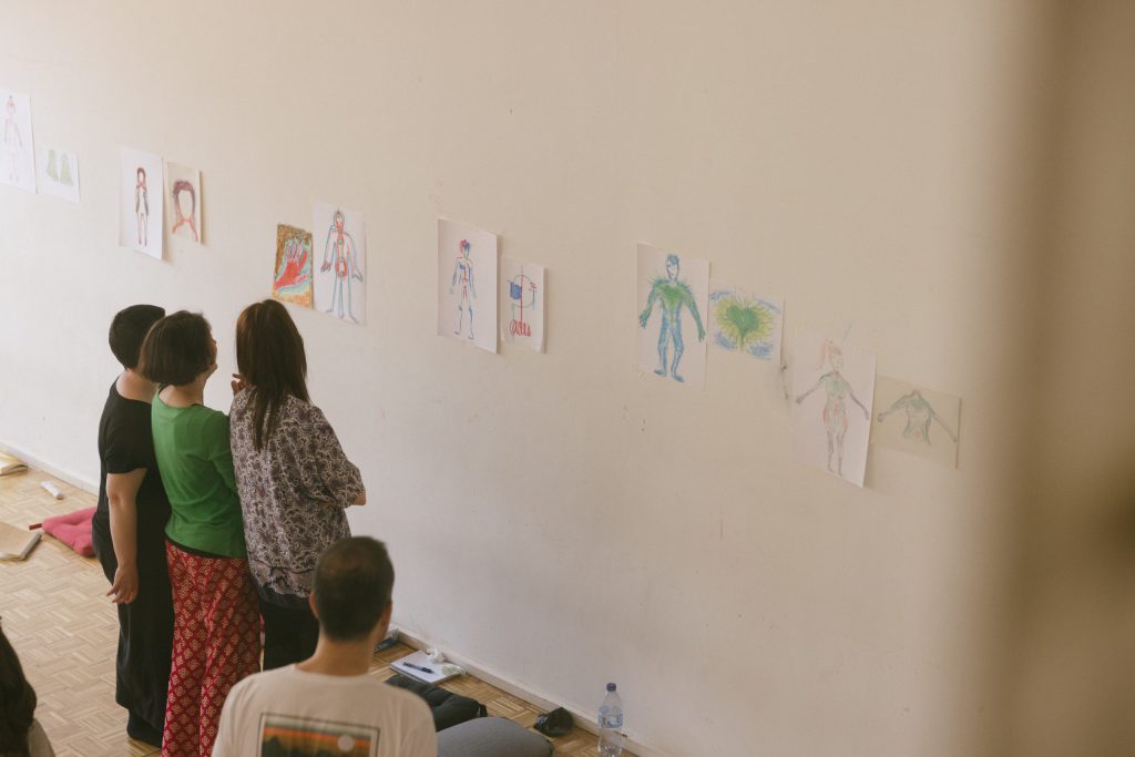 Estudiantes del máster de Arteterapia Gestalt observan y comentan dibujos del cuerpo humano colgados en la pared.